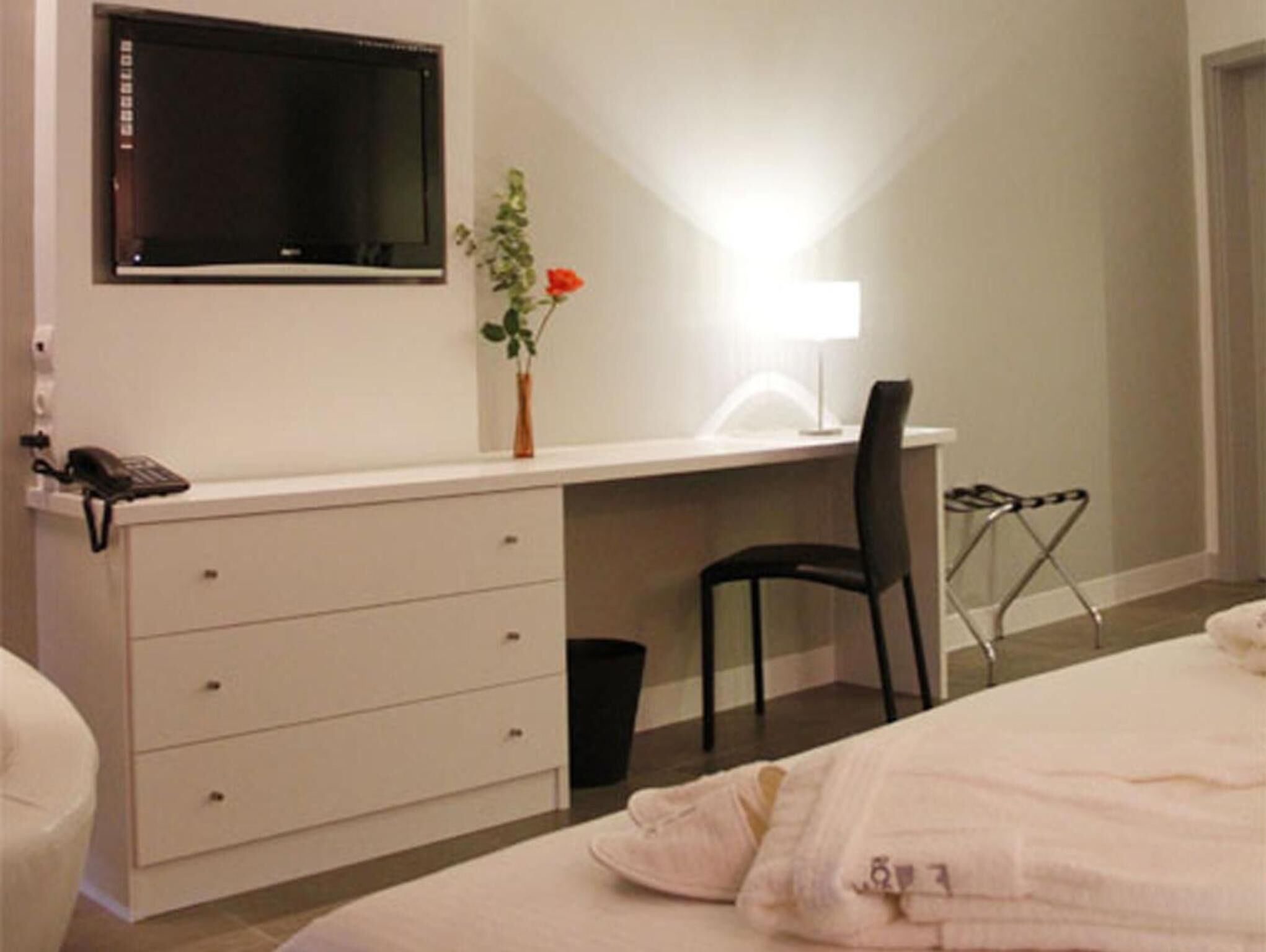 Quarto com uma cama, escrivaninha com cadeira, televisão e uma pequena planta.