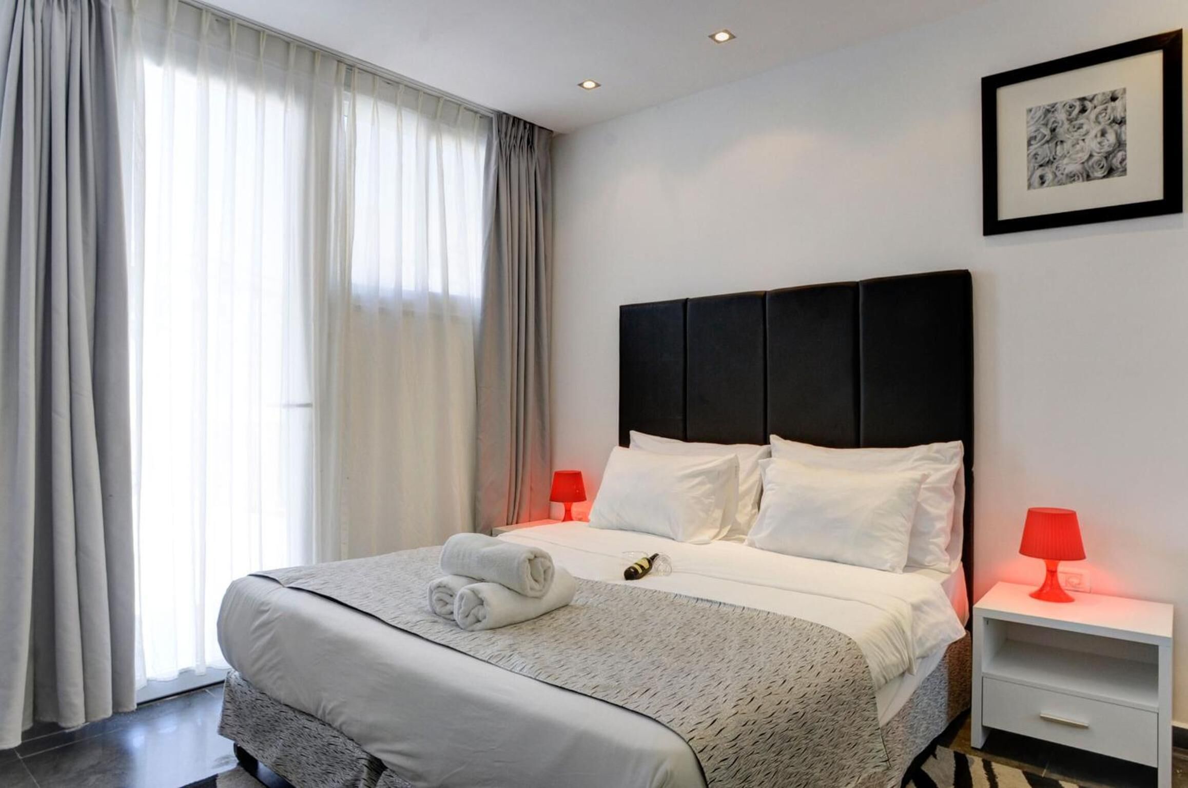 A hotel room with a large bed, two bedside tables, a framed picture on the wall, and a window with curtains.