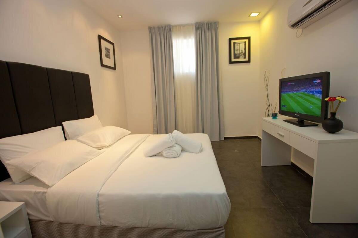 A hotel room with a neatly made bed, a desk with a television, and a window with curtains.