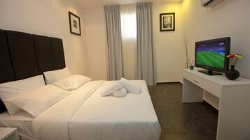 A hotel room with a neatly made bed, a desk with a television, and a window with curtains.