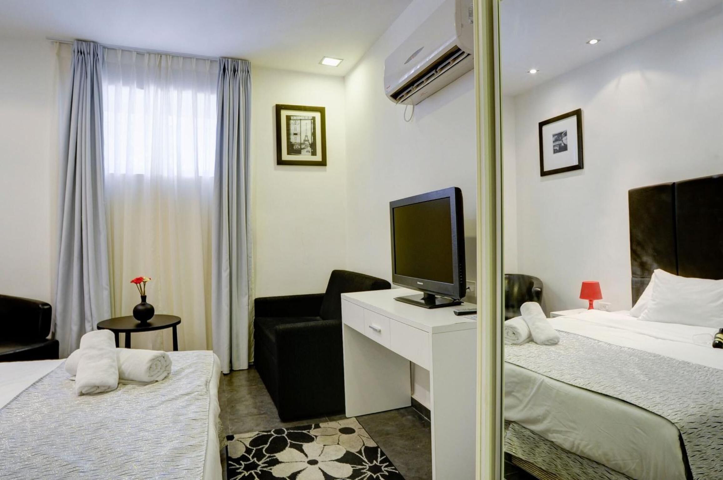 A hotel room with two beds, a desk, a chair, a television, and an air conditioning unit.