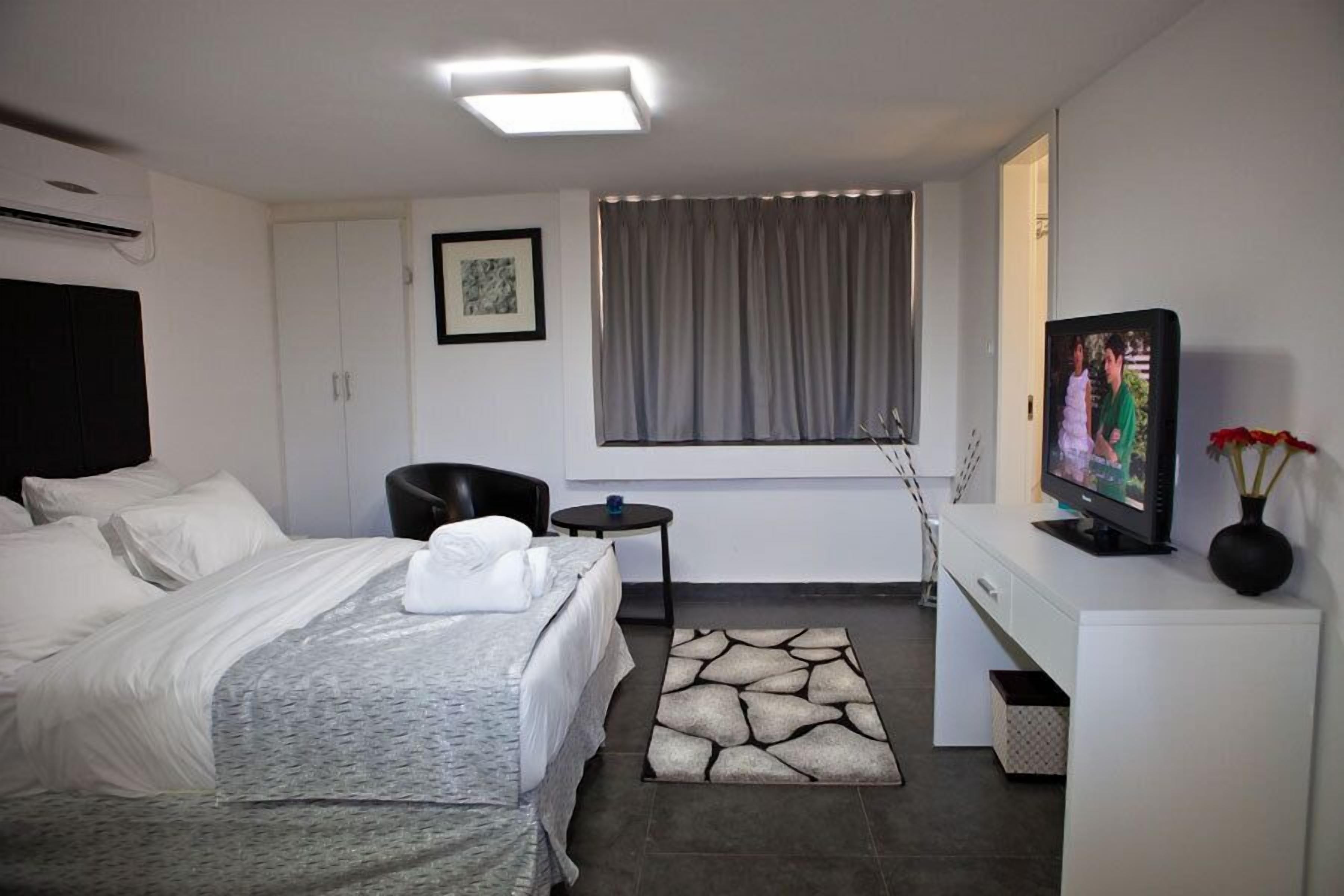Een hotelkamer met een bed, een bureau met een televisie, een stoel, een klein tafeltje en een raam met gordijnen.
