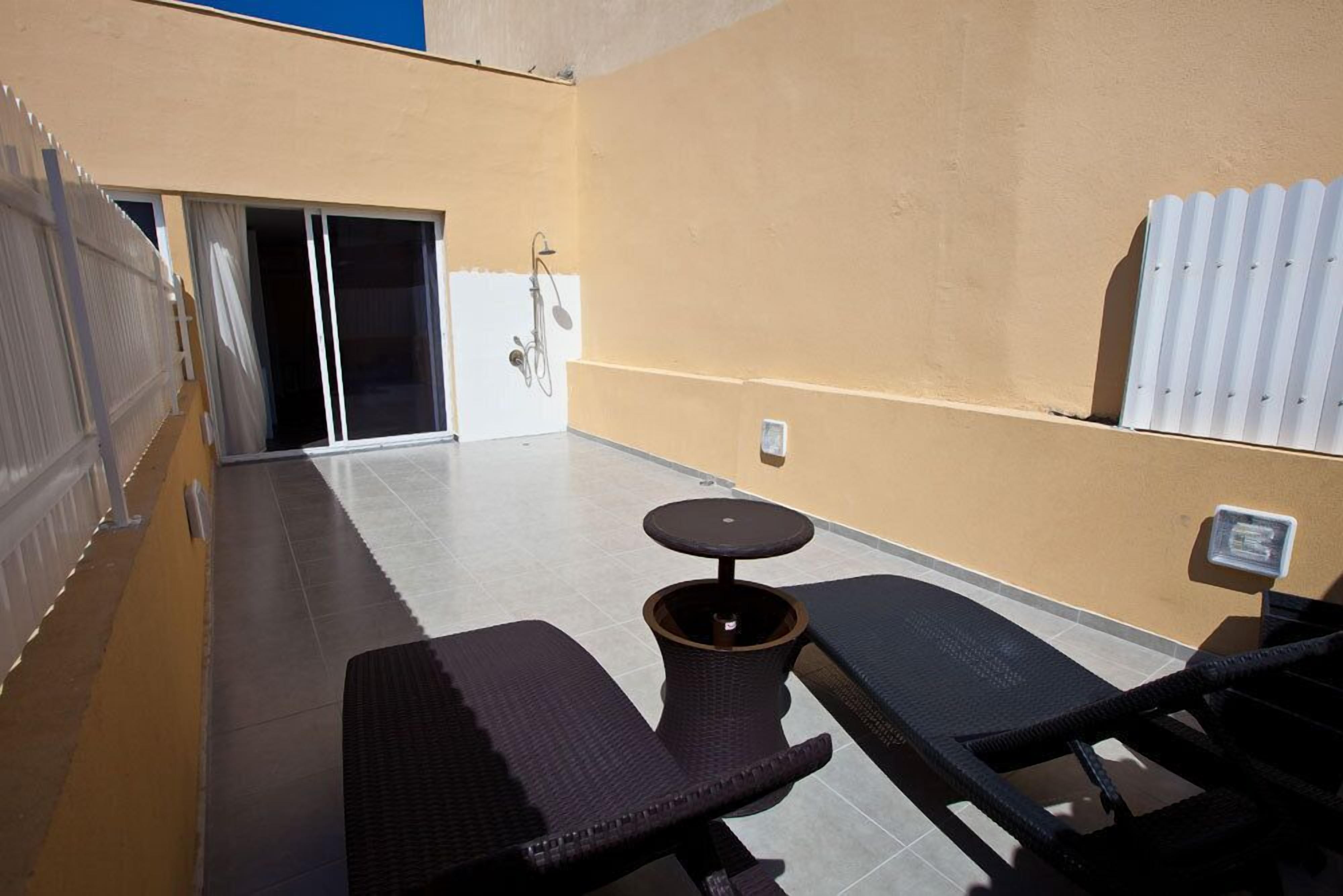 Un patio soleado con una pequeña mesa y dos sillones, una puerta corrediza de vidrio y un radiador blanco.