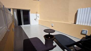 Un patio soleado con una pequeña mesa y dos sillones, una puerta corrediza de vidrio y un radiador blanco.