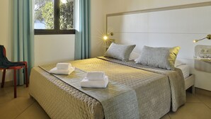 A neatly made bed with a folded towel, a bedside table with glasses, and a window with curtains. - Résidence Arco Plage (Olmeto)