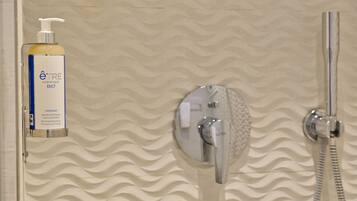 Un baño con pared texturizada, ducha con cabezal de ducha manual y una botella de champú orgánico.
