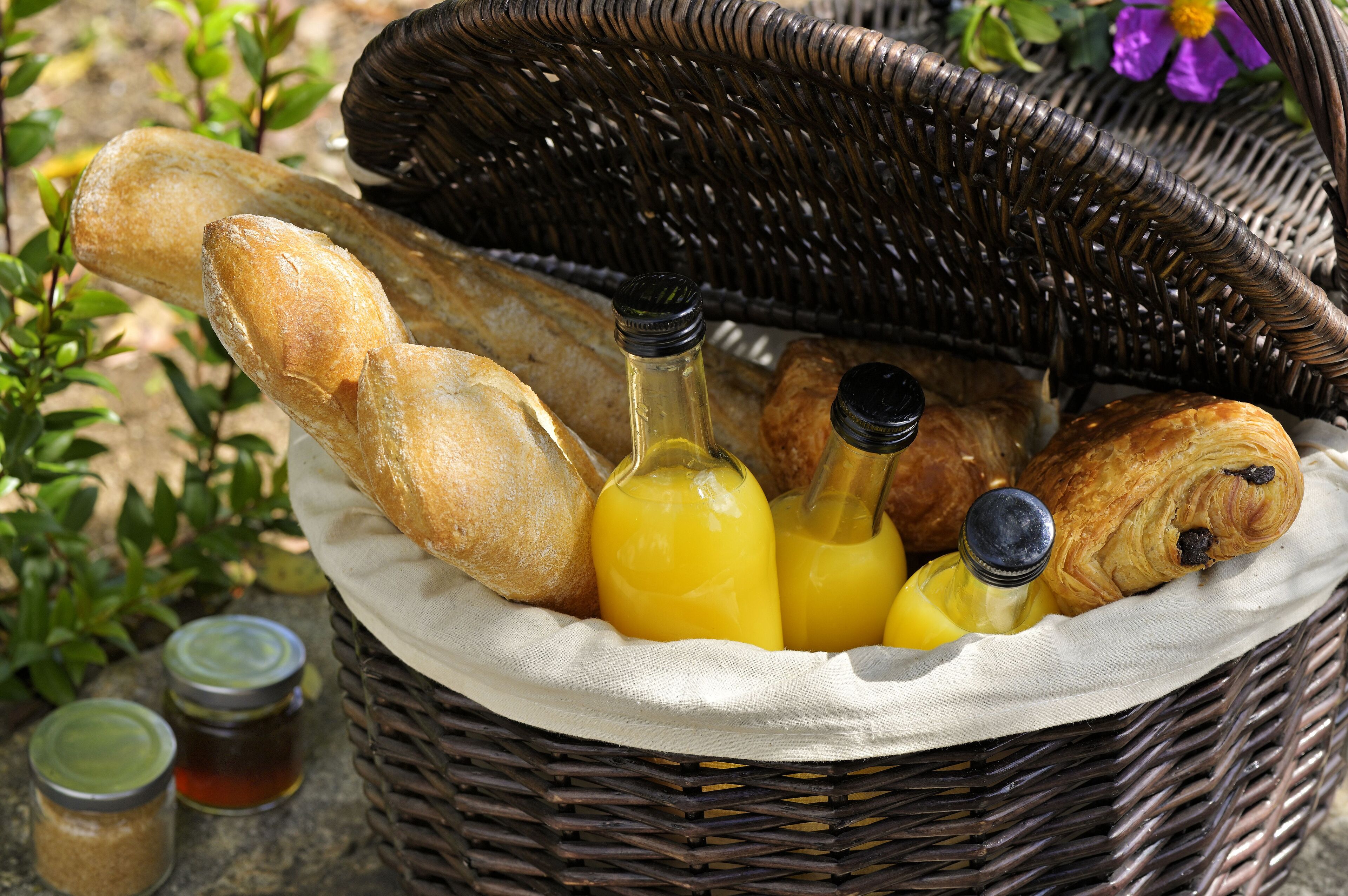 A wicker basket containing bread, bottles of orange juice, and jars of condiments.
