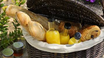 A wicker basket containing bread, bottles of orange juice, and jars of condiments.