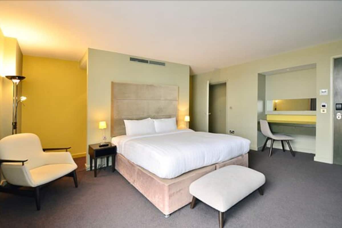 Ein Hotelzimmer mit einem großen Bett, einem Sessel, einem Schreibtisch und einem Spiegel.