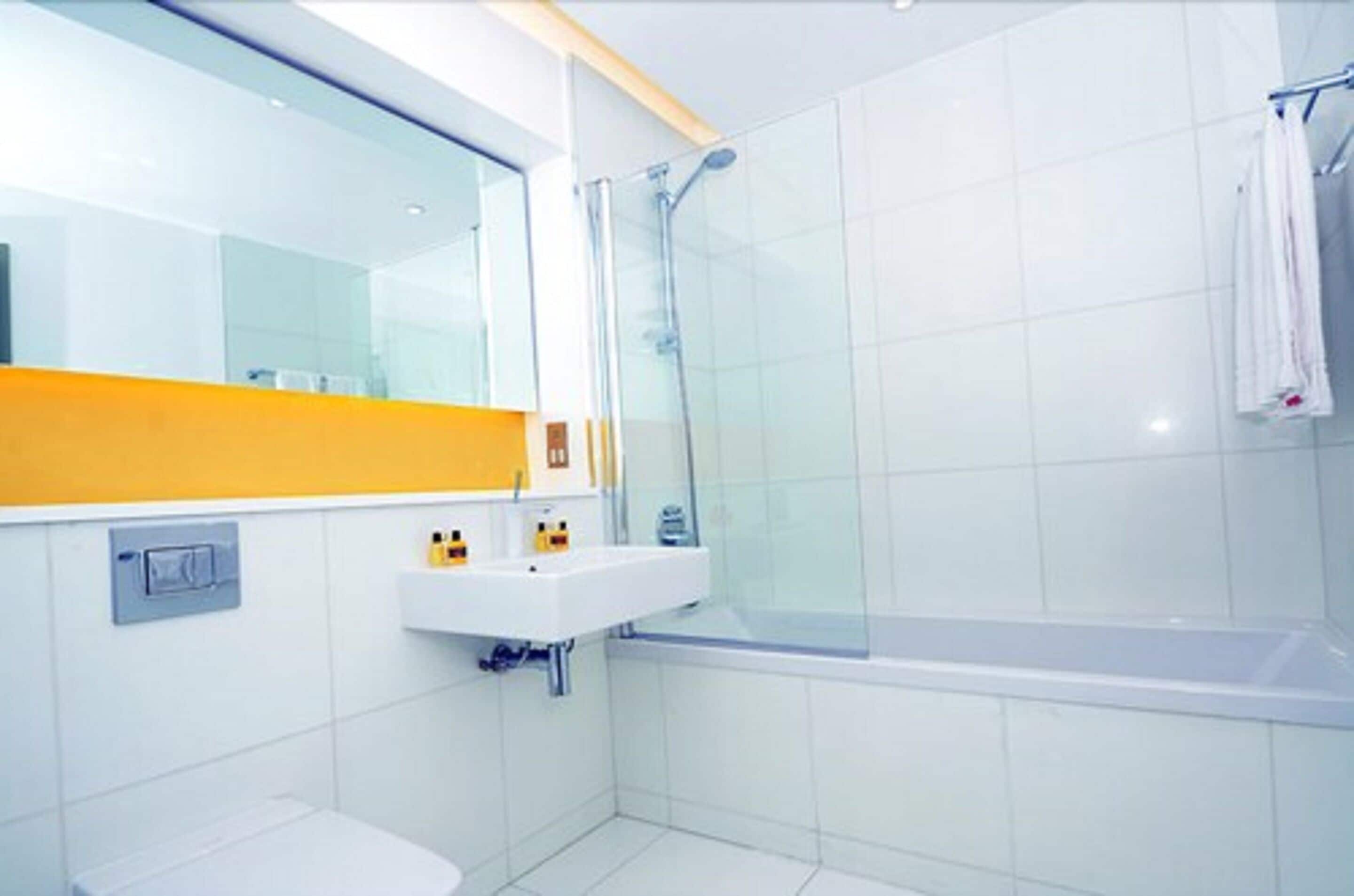 Une salle de bain moderne avec une douche à parois de verre, un lavabo blanc et un mur d’accent jaune.