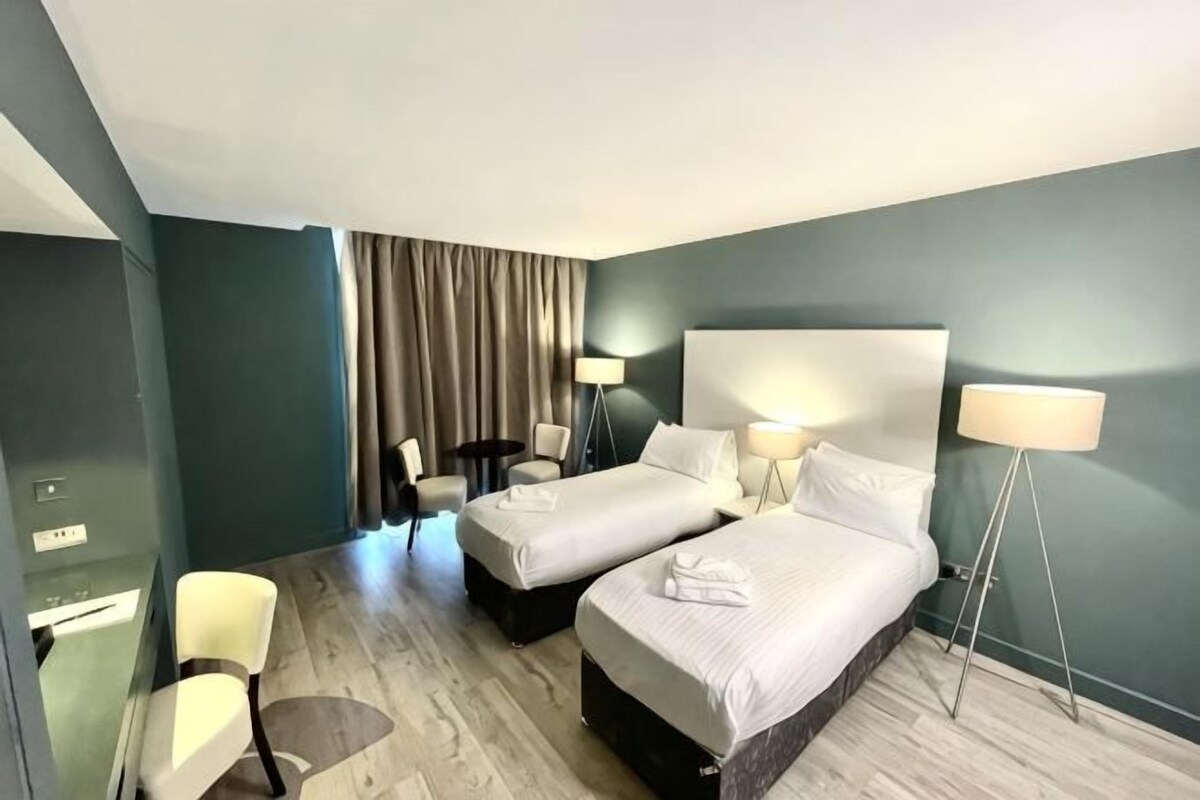 Una habitación de hotel con dos camas, un escritorio, una silla y una lámpara.