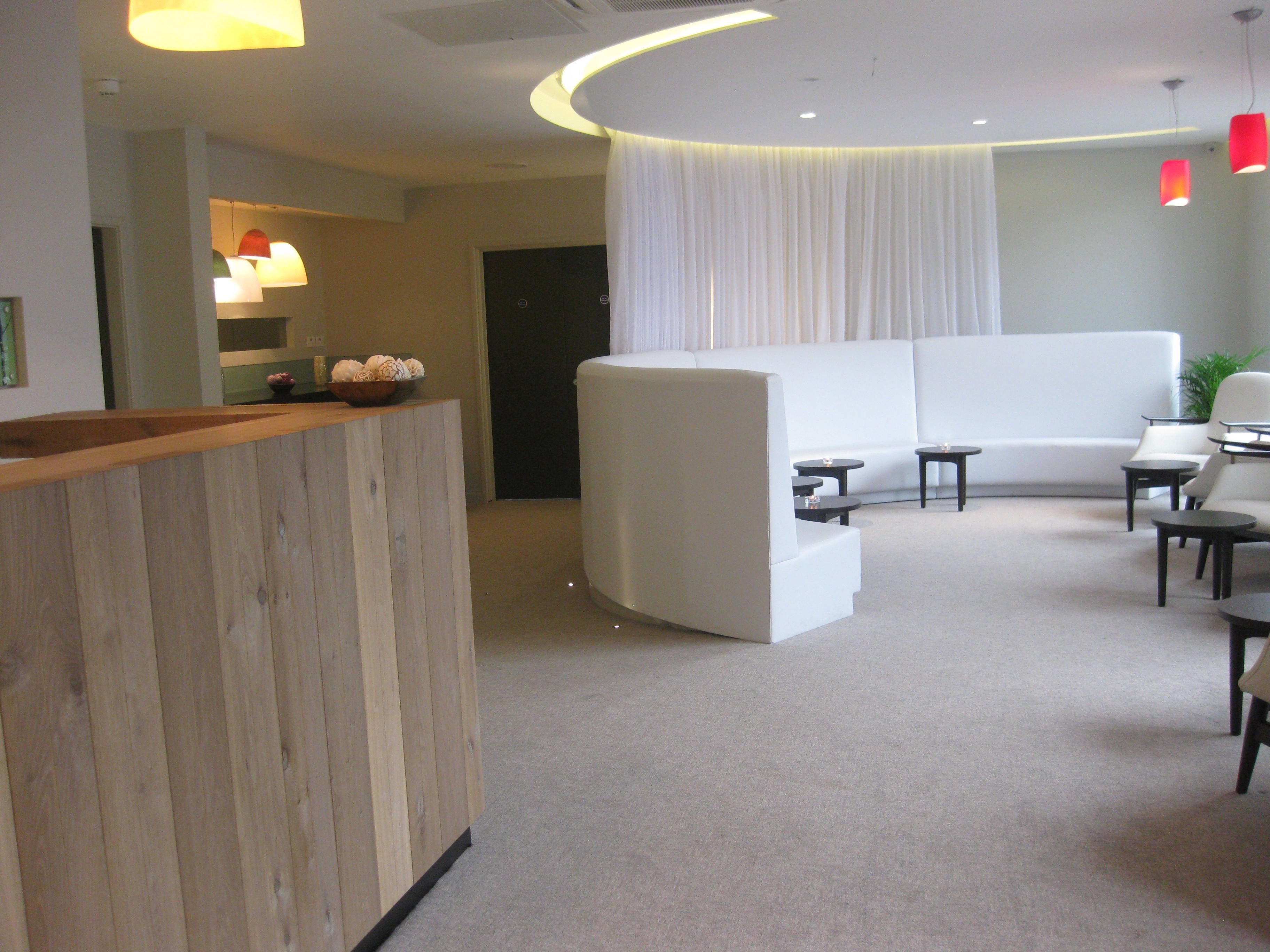 A modern hotel lobby with a reception desk, a seating area with sofas and tables, and a large window with curtains.
