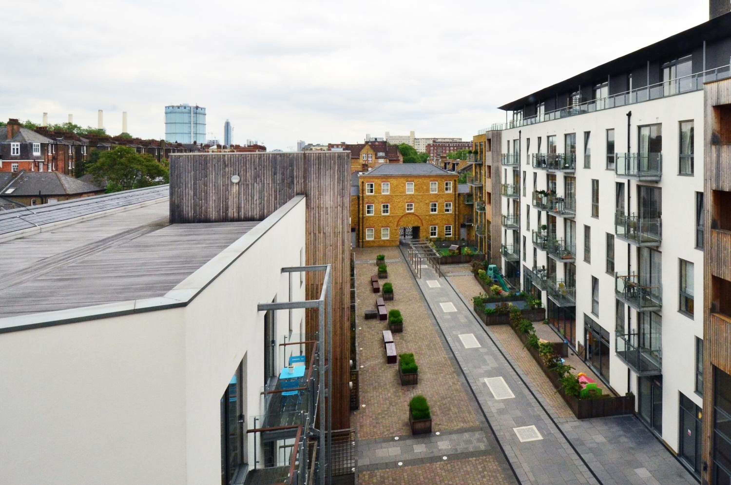 A modern urban building with a rooftop terrace, a central courtyard with seating, and a mix of residential and commercial buildings in the background.
