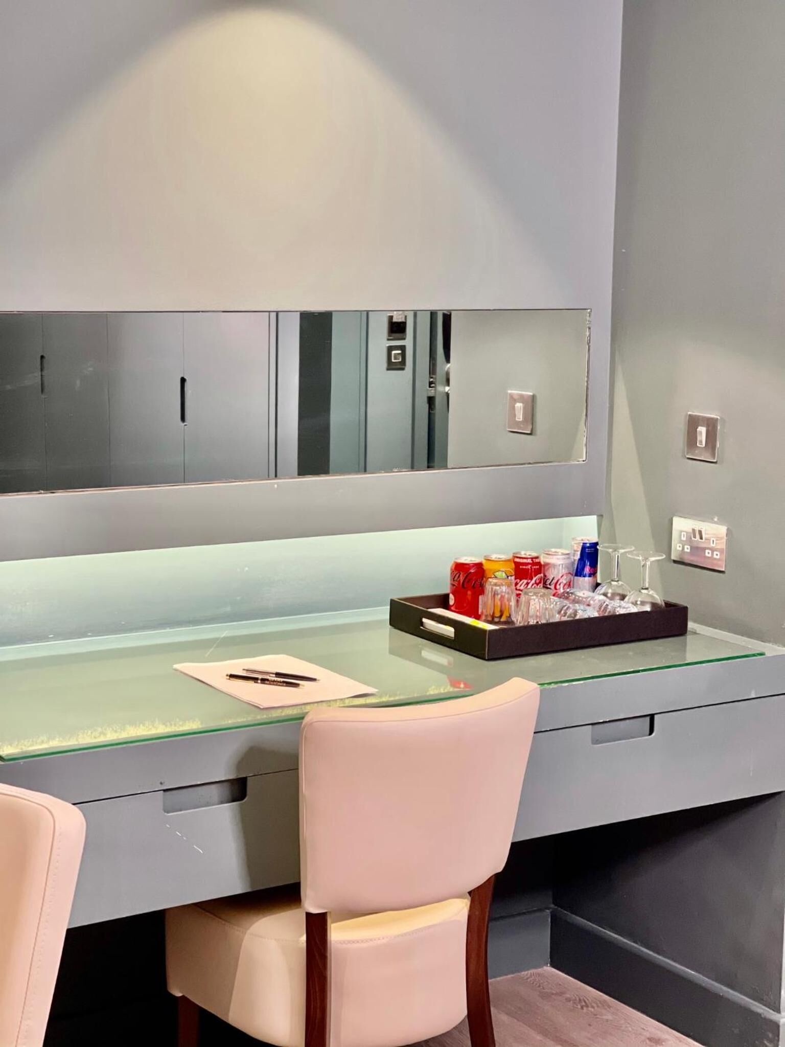 A modern office space with a glass desk, a white chair, and a mirror above the desk.