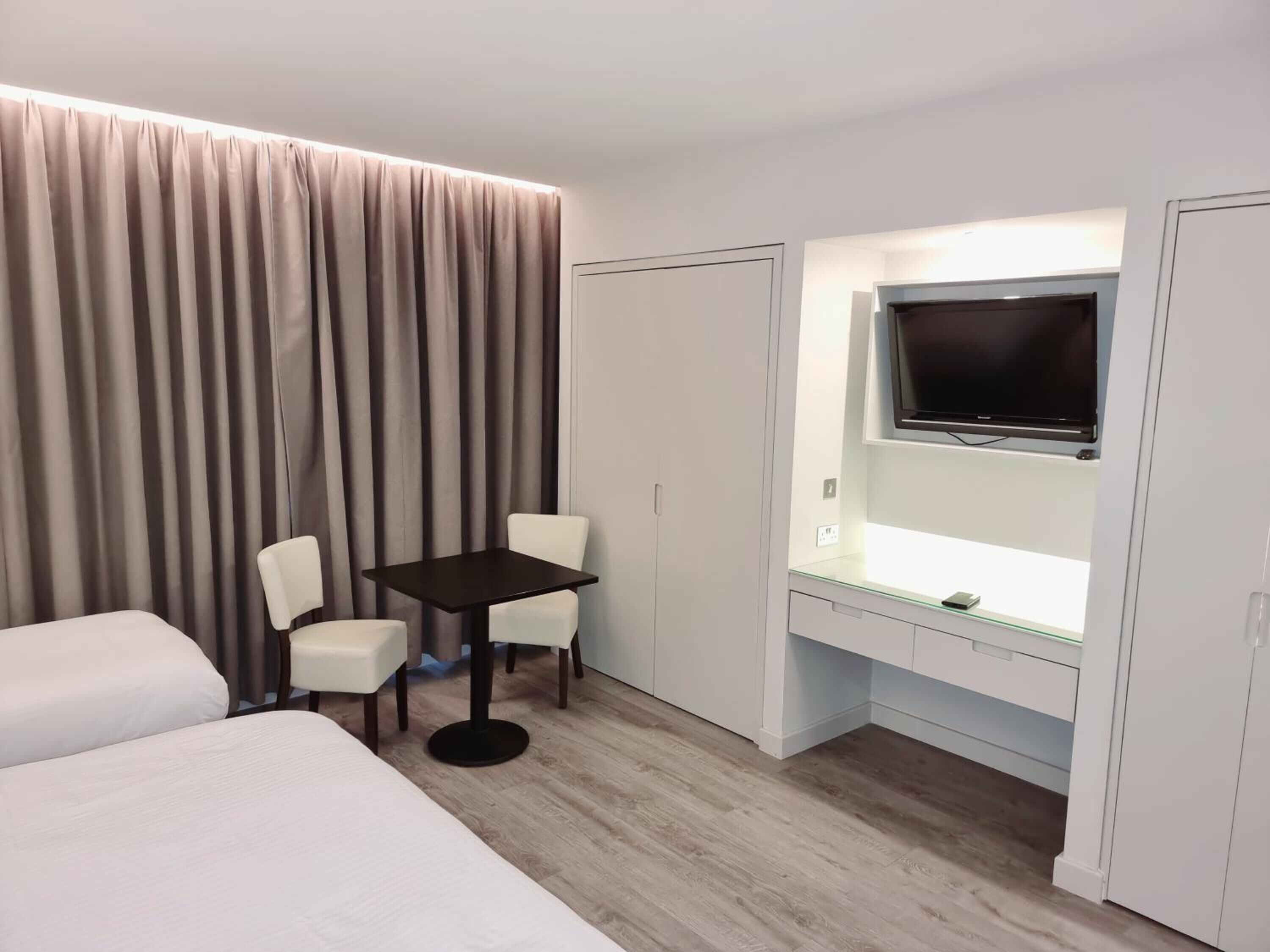 A hotel room with a bed, a desk with a chair, a TV, and curtains.