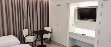 A hotel room with a bed, a desk with a chair, a TV, and curtains.