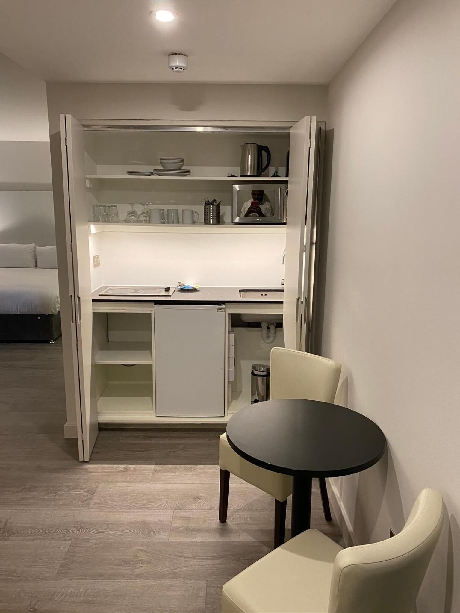A compact kitchen with a microwave, coffee maker, and a small refrigerator. There is a dining table with two chairs.