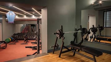 Een sportschool met gewichthefapparatuur, een bank en een spiegel aan de muur.