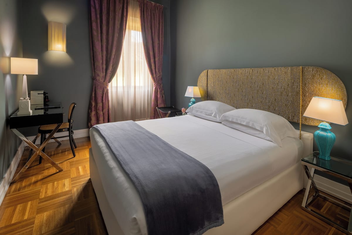 Habitación de hotel con una cama grande, dos lámparas de noche, un escritorio con silla y una ventana con cortinas.