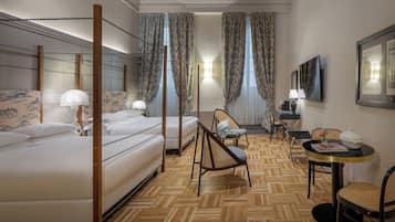 Une chambre d’hôtel avec un lit à baldaquin, un coin salon avec une table et des chaises, et une grande fenêtre avec des rideaux.