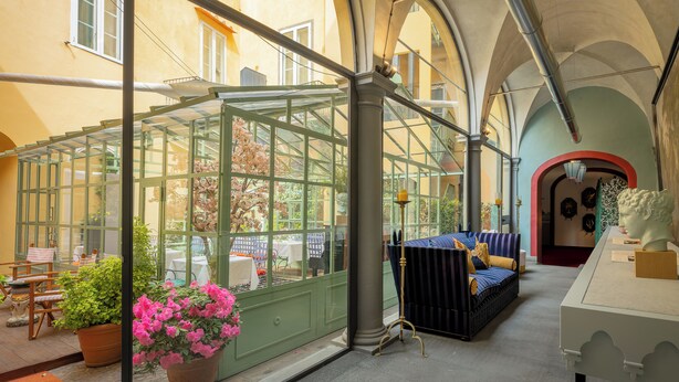 A conservatory with glass walls, a sofa, and a bust sculpture. - Hotel Number Nine (Florence)