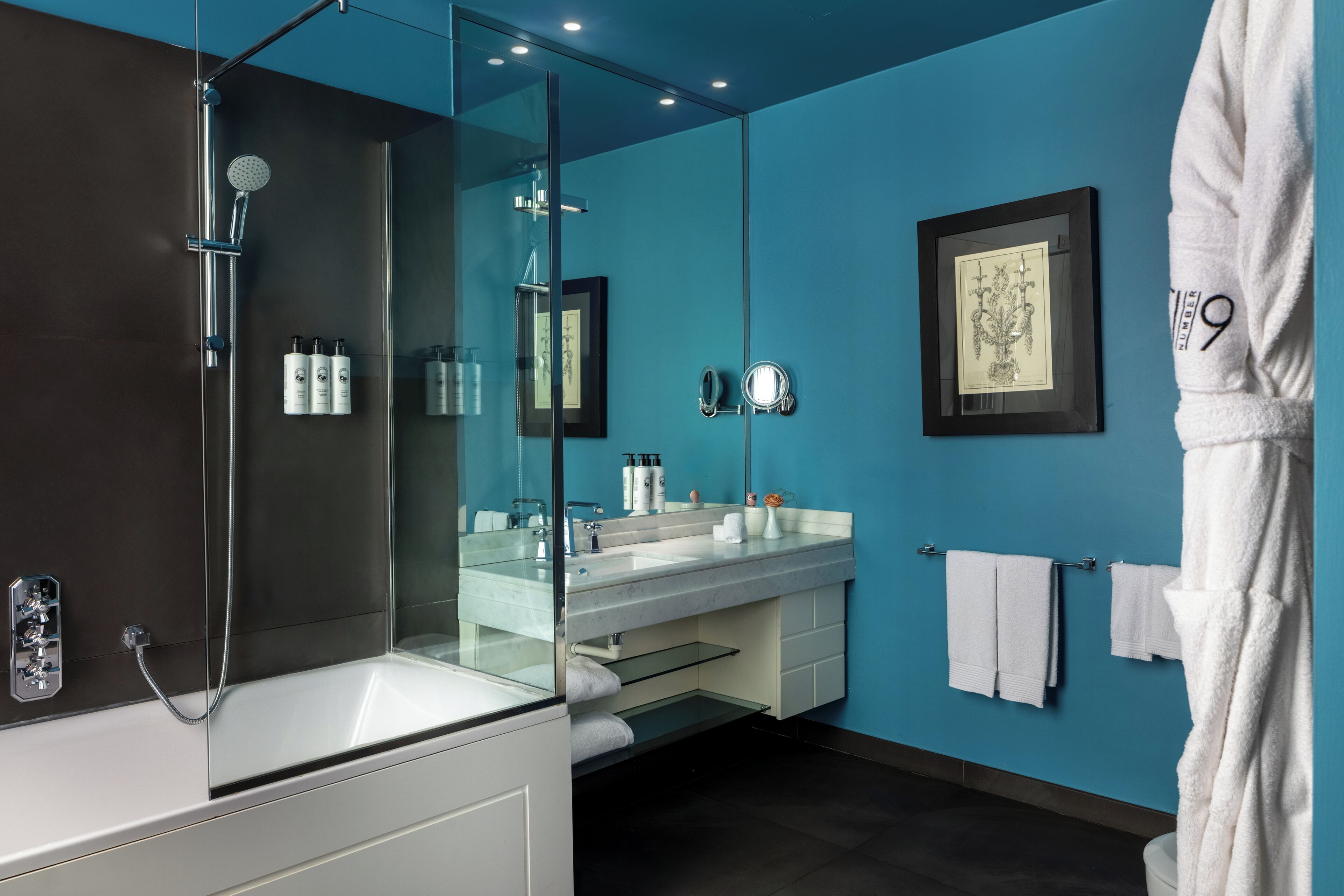 Un baño moderno con cabina de ducha de vidrio, tocador blanco con espejo grande y pared de acento azul.