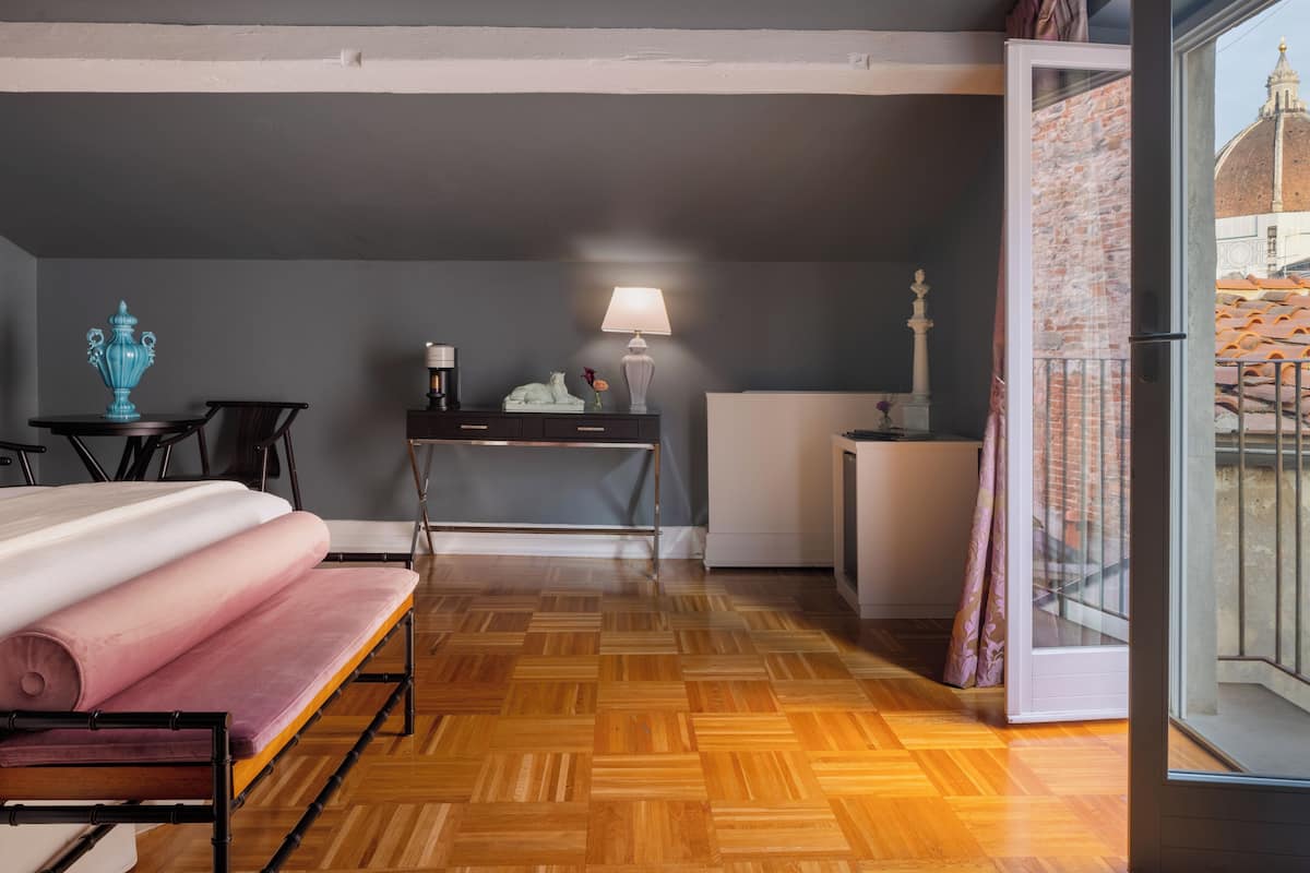 Habitación de hotel con cama, escritorio, lámpara y vista a un paisaje urbano a través de una ventana.
