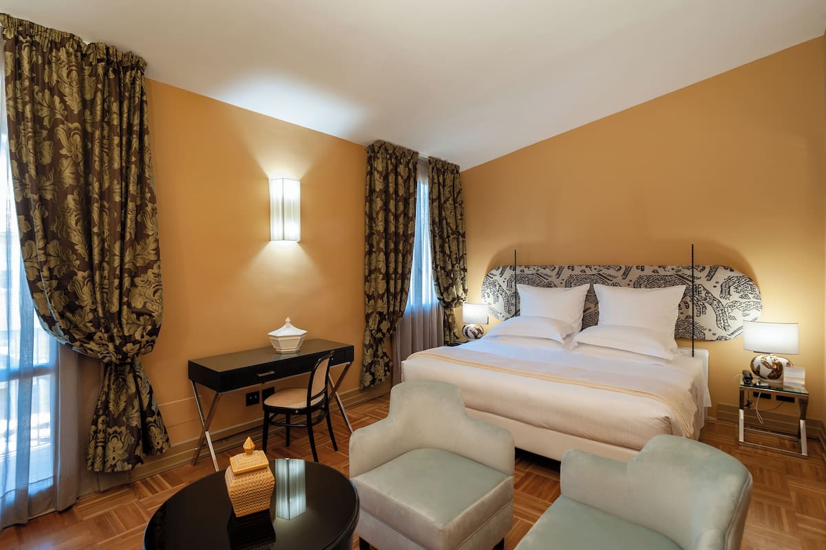Una habitación de hotel con una cama, dos sillones, un escritorio y una lámpara.
