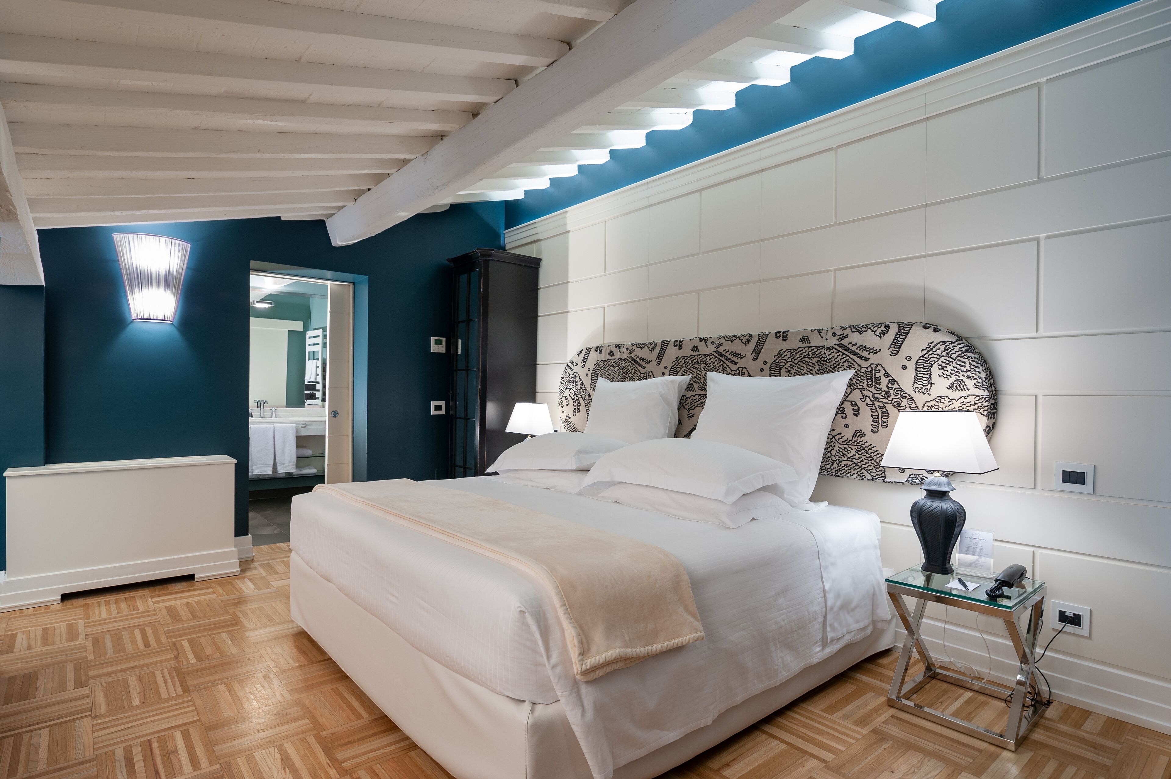 A bedroom with a large bed, a bedside table with a lamp, and a mirror.