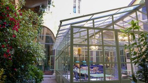A greenhouse with a glass roof, surrounded by greenery and a pathway leading to a seating area with tables and chairs. - Hotel Number Nine (Florence)