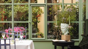 A conservatory with a piano, a table set with wine glasses, and a bust sculpture. - Hotel Number Nine (Florence)