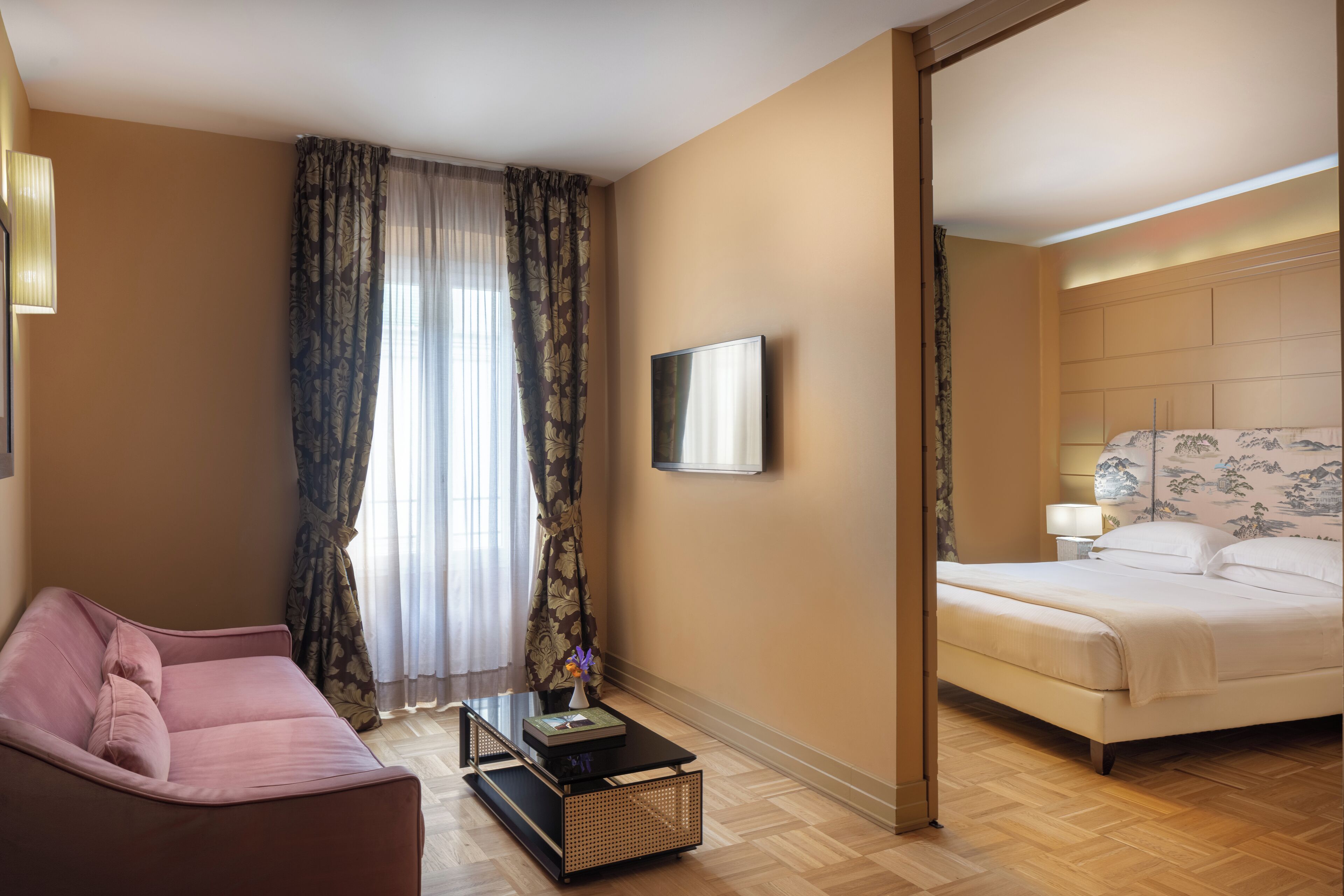 A hotel room with a bed, a sofa, a TV, and a window with curtains.