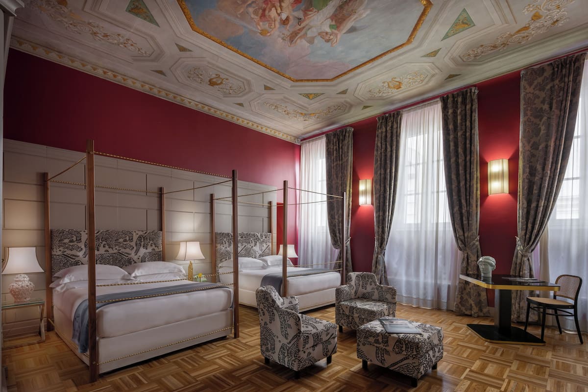 Una cama con dosel y cuatro columnas, un espacio de estar con sillones estampados y una mesa con lámpara.