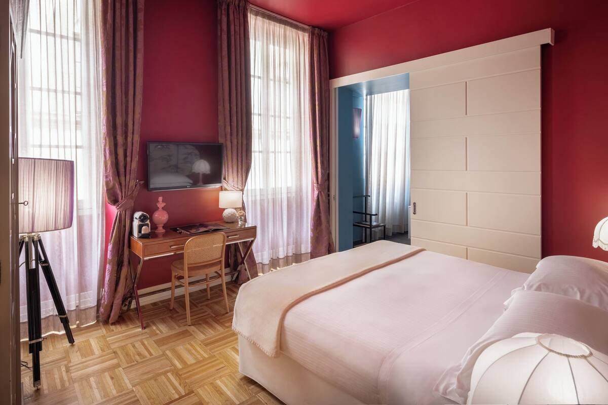 Un dormitorio con cama, escritorio, silla, televisor y cortinas.