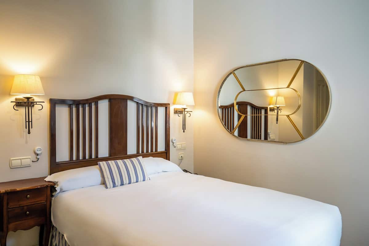 A neatly made bed with a wooden headboard, two bedside lamps, and a round mirror on the wall.