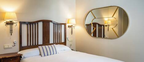 A neatly made bed with a wooden headboard, two bedside lamps, and a round mirror on the wall.