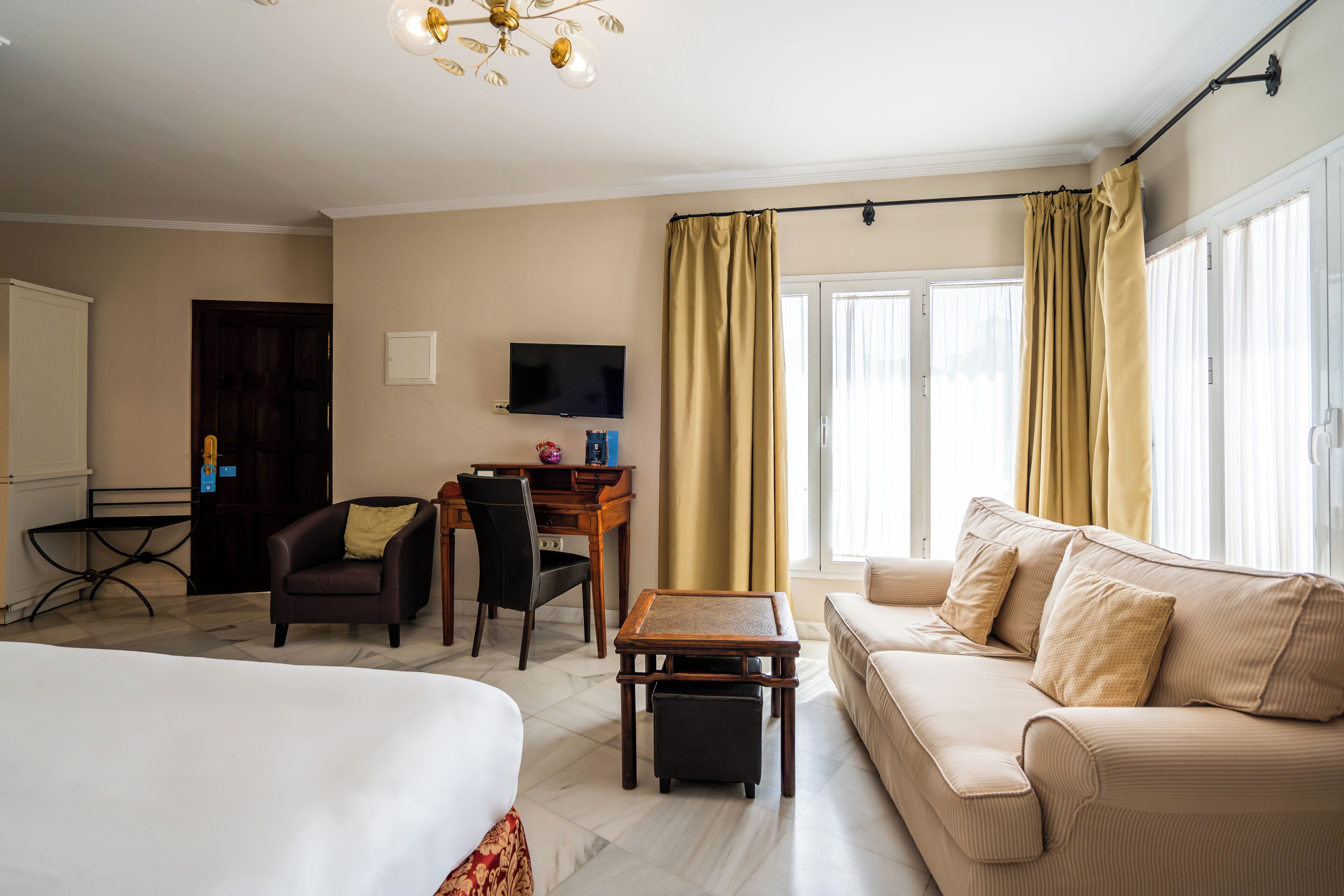 Een hotelkamer met een bed, een slaapbank, een bureau met stoel, een televisie en gordijnen.