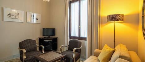 Una sala de estar con un sofá, dos sillones, una mesa de centro, un televisor y una lámpara.