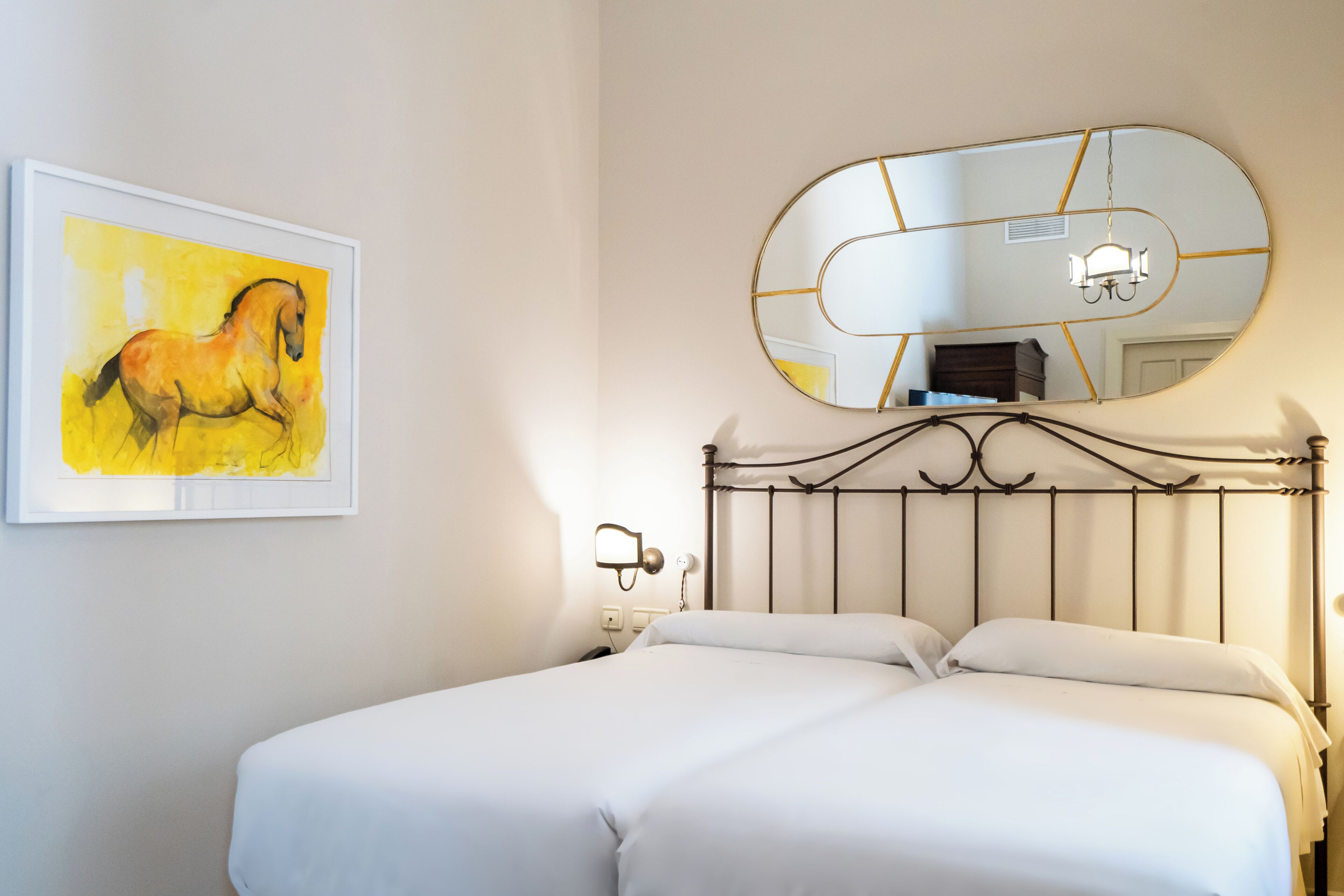 A bedroom with a bed, a wall-mounted mirror, and a framed painting of a horse.