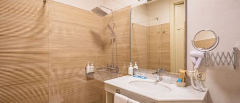 A modern bathroom with a wooden panel wall, a glass shower enclosure, a white sink with a mirror, and a hairdryer mounted on the wall.