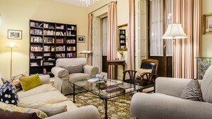 Un salon comprenant un canapé, des fauteuils, une table basse, une bibliothèque et un lustre.