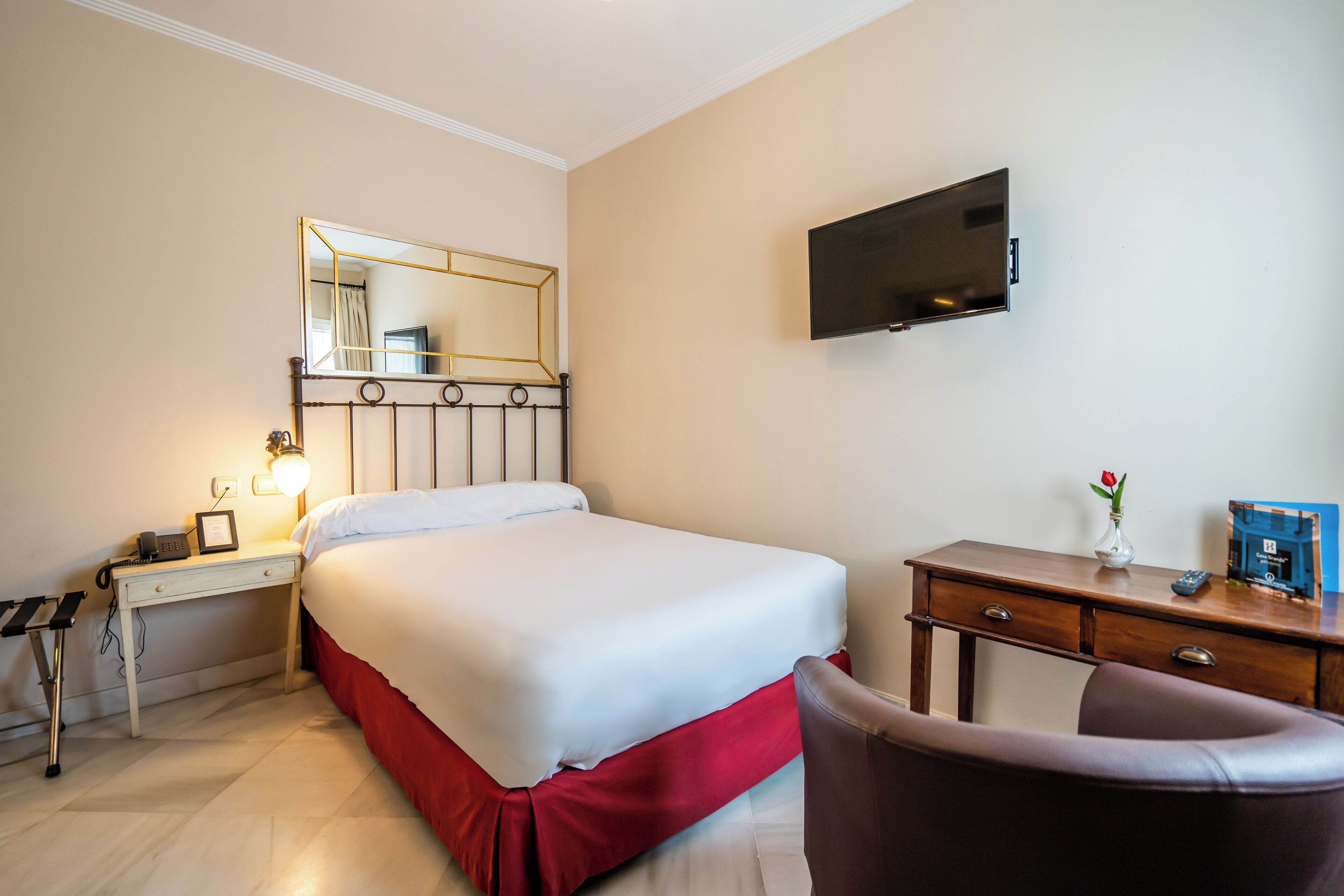 Une chambre d’hôtel avec un lit, une table de chevet, une lampe, une télévision et une chaise.
