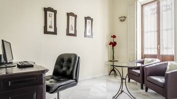 Una oficina moderna con escritorio, sillón de cuero, dos sillones, una mesa de cristal y cuadros en la pared.