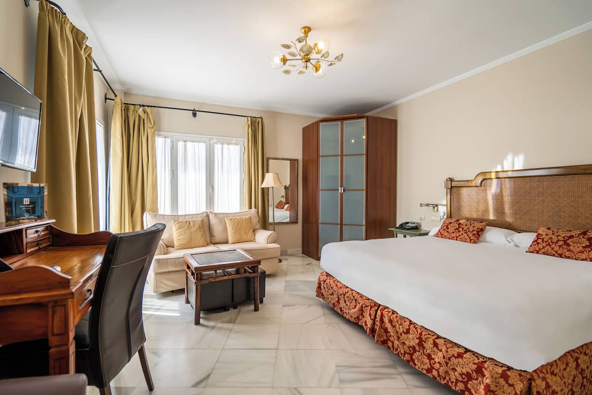 A hotel room with a bed, a desk, a chair, a sofa, a wardrobe, and a television.