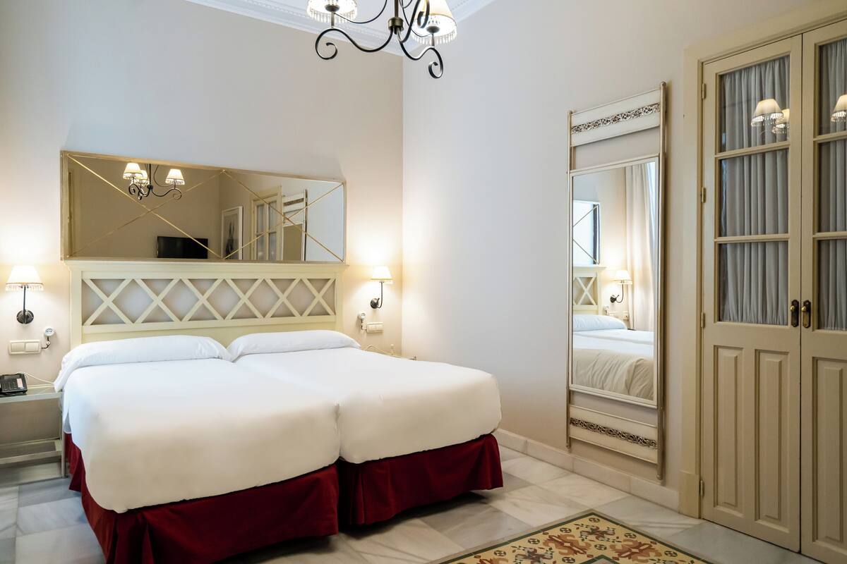 A double bed with white linens, a large mirror above it, and a chandelier.