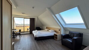 A modern hotel room with a large bed, a desk, and a chair. There is a balcony with a view of the city. - Hotel 't Zwaantje (Callantsoog)