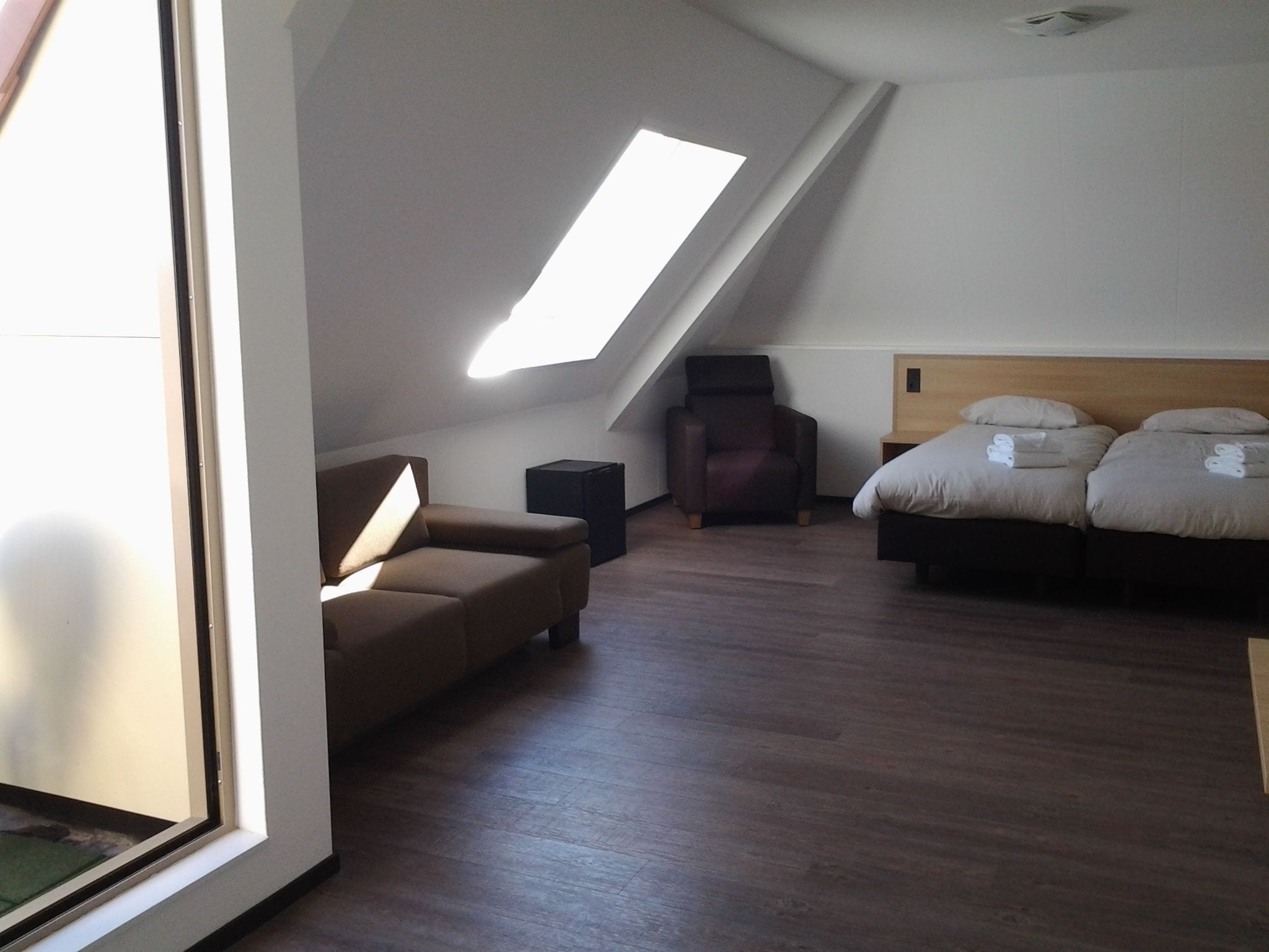 A bedroom with a sloped ceiling, a sofa, a chair, a bed with pillows, and a small table.