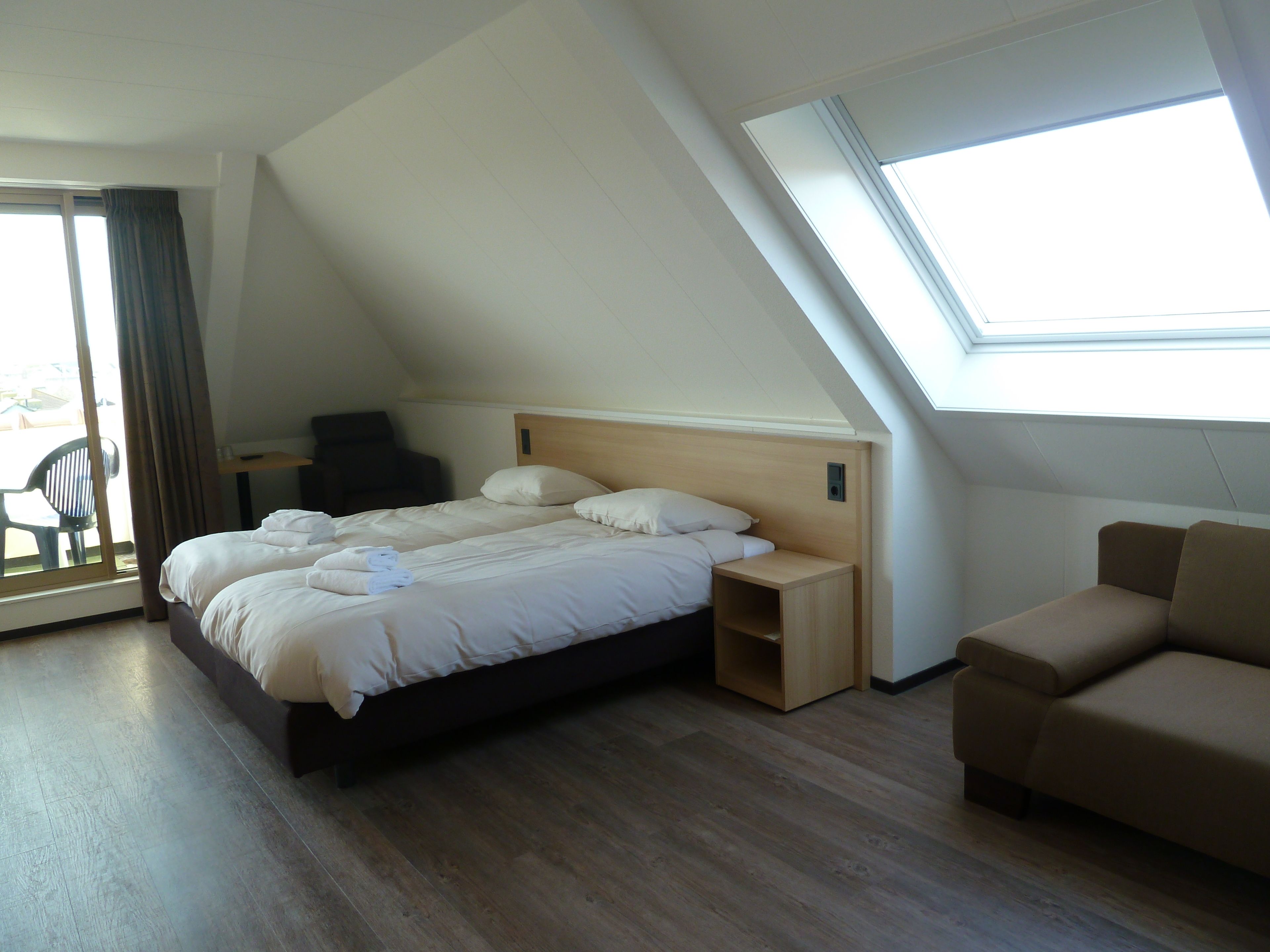 Une chambre d’hôtel moderne avec un grand lit, un canapé, un bureau et une fenêtre de toit.