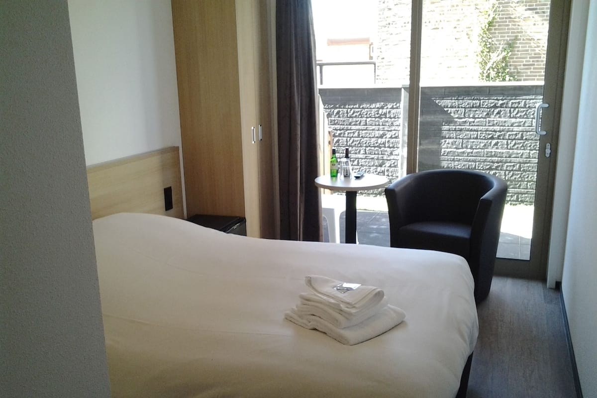 A hotel room with a bed, a chair, a small table, and a view of the outside.