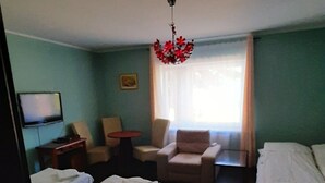Quarto de hotel com duas camas de solteiro, um sofá, uma poltrona, uma televisão e um candelabro.